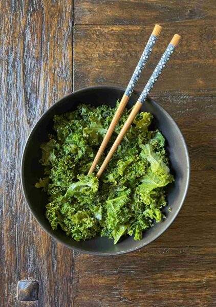 Simply Beautiful kale in a black bowl with warm wood and chopsticks